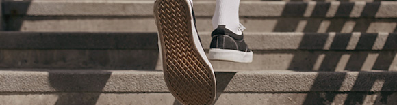 Rear view of a pair of feet wearing sneakers and crew length socks climbing a set of concrete stairs outdoor on a sunny day