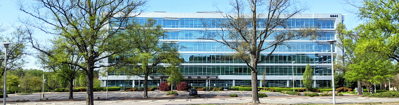 a six-floor office building with a large tree-studded parking lot in the foreground