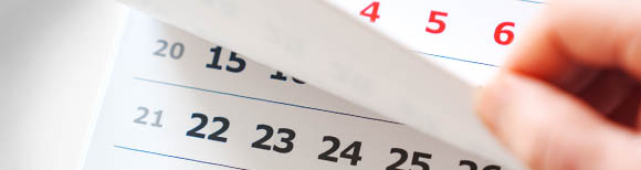 A hand on the right flips a page up on a paper calendar.