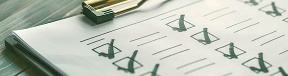 A checklist in several columns secured by a clipboard rests on a tabletop.