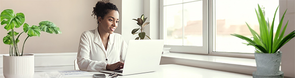 A woman works on a laptop while seated at a desk in a bright, minimalist office.