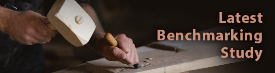 An image of a man's hands holding a mallet and chisel, making carved marks into a woden board resting on a workbench. On the right side of the image is text which reads Latest Benchmarking Study.
