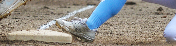 A lower leg and foot wearing a baseball sock and shoe. The foot is resting on a baseball base.