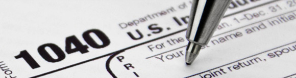 The tip of a writing pen filling in a paper IRS 1040 tax form.