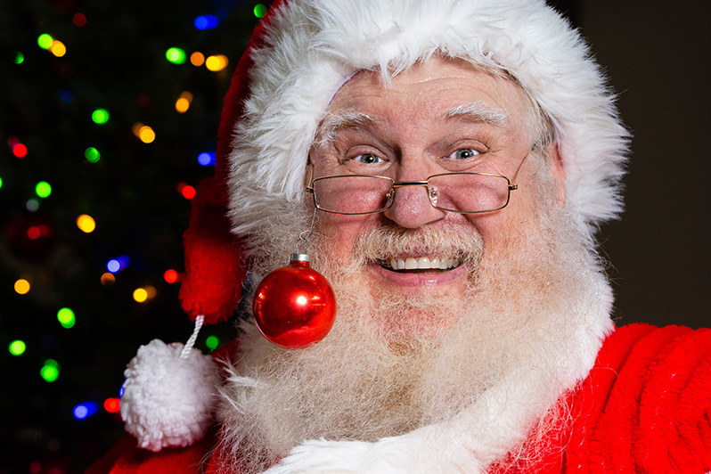 Joe Kapelewski dressed as Santa Claus with holiday lights behind him